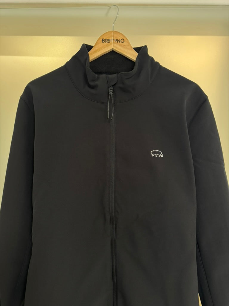 Black breitung jacket with a small logo on a hanger against a beige wall.