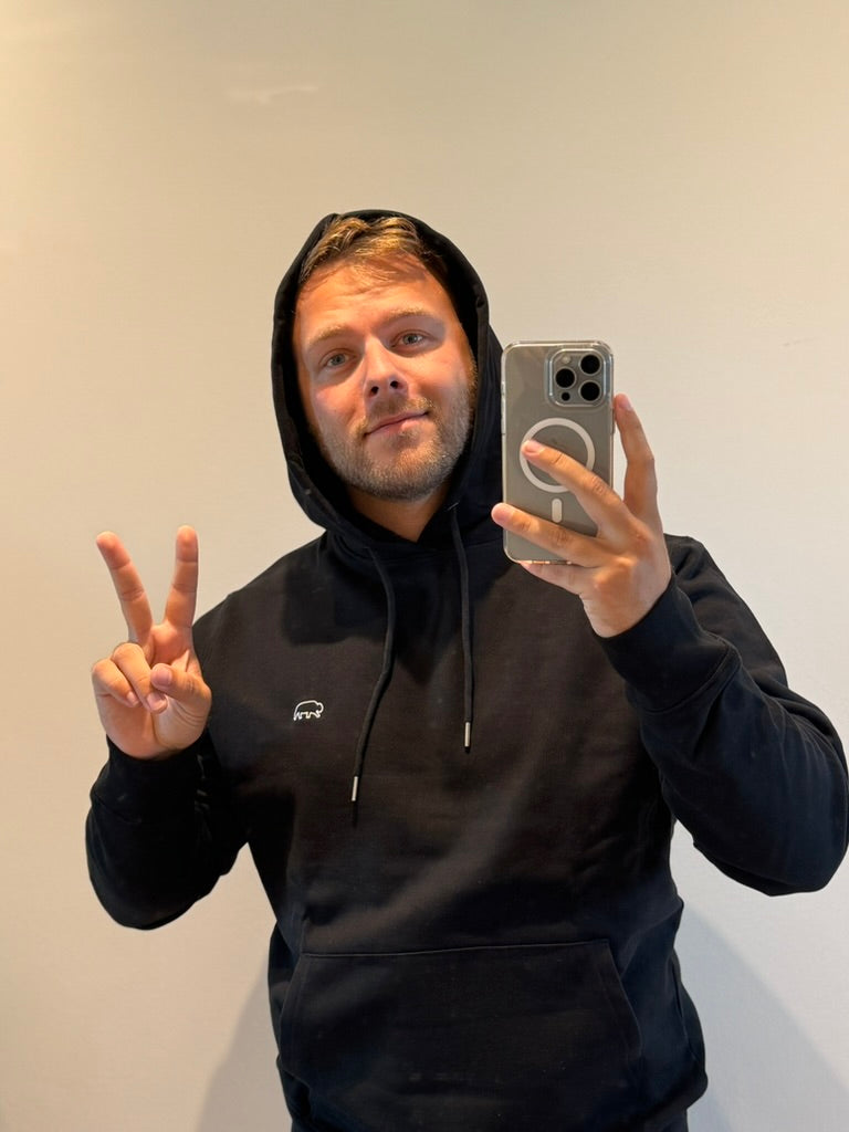 Man in a black breitung hoodie taking a mirror selfie with a phone.