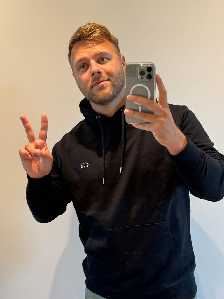 Man taking a mirror selfie wearing a black Breitung hoodie with a logo, making a peace sign.