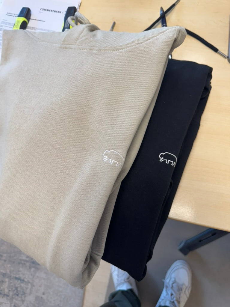 Beige and black Breitung hoodies with a bison logo on a wooden surface