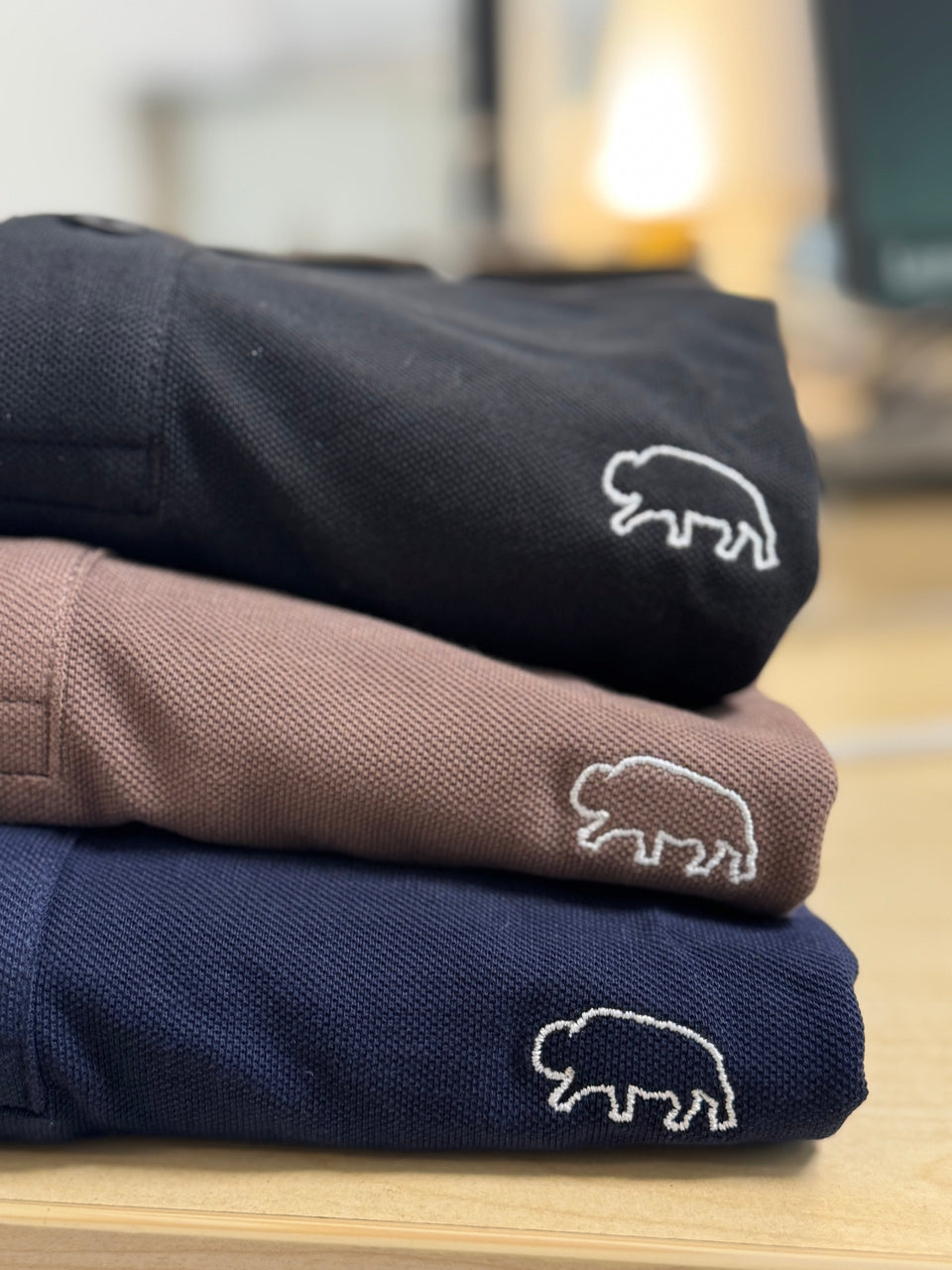 Stack of folded breitung polo shirts with white bison oulineembroidered logo on a wooden surface